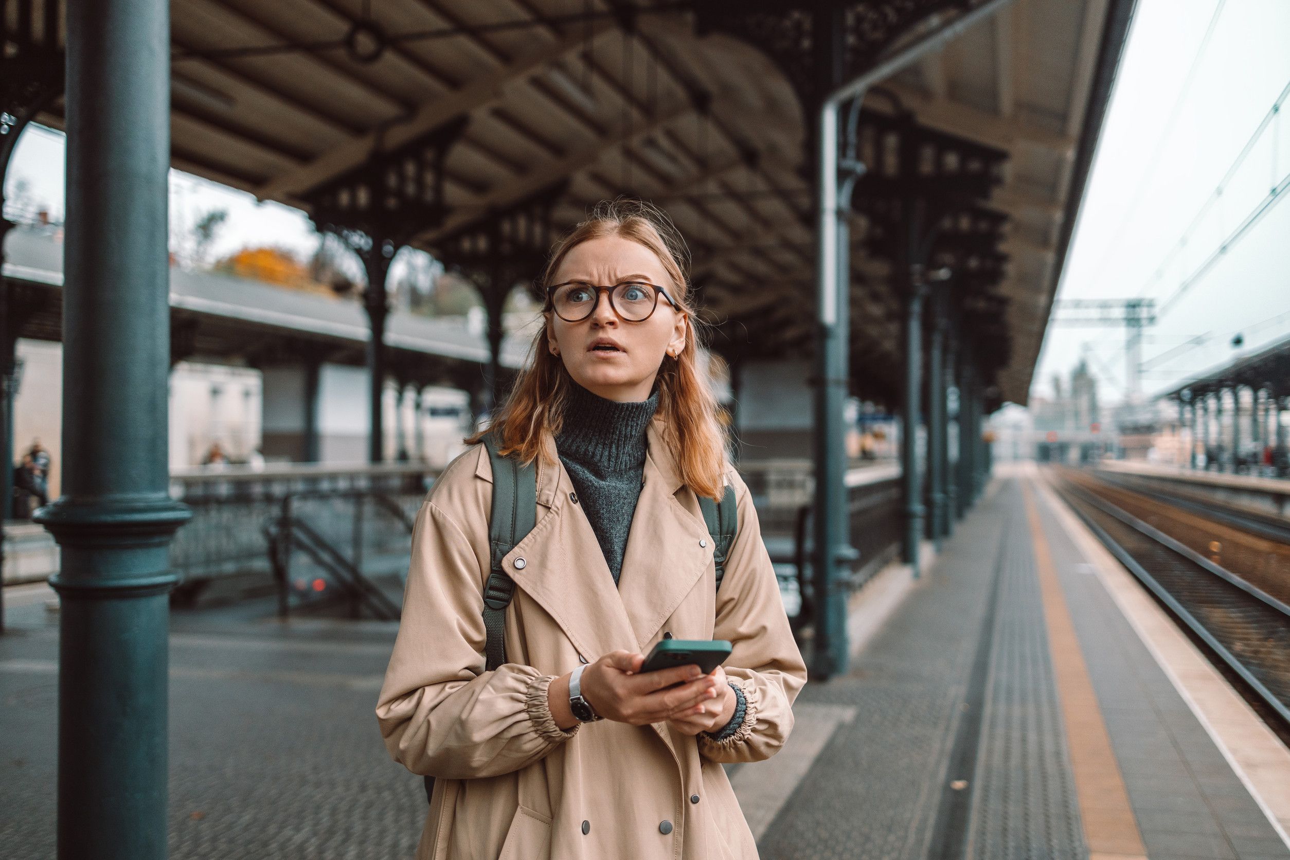 Mujer perdida y enojada, parada sola en el andén del tren, esperando al aire libre.