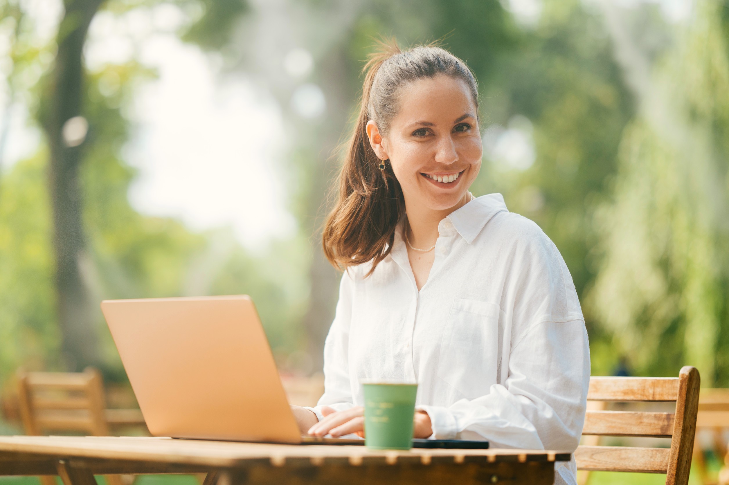 Hübsche junge Frau genießt die Arbeit im Freien auf einer Café-Terrasse in einem Park