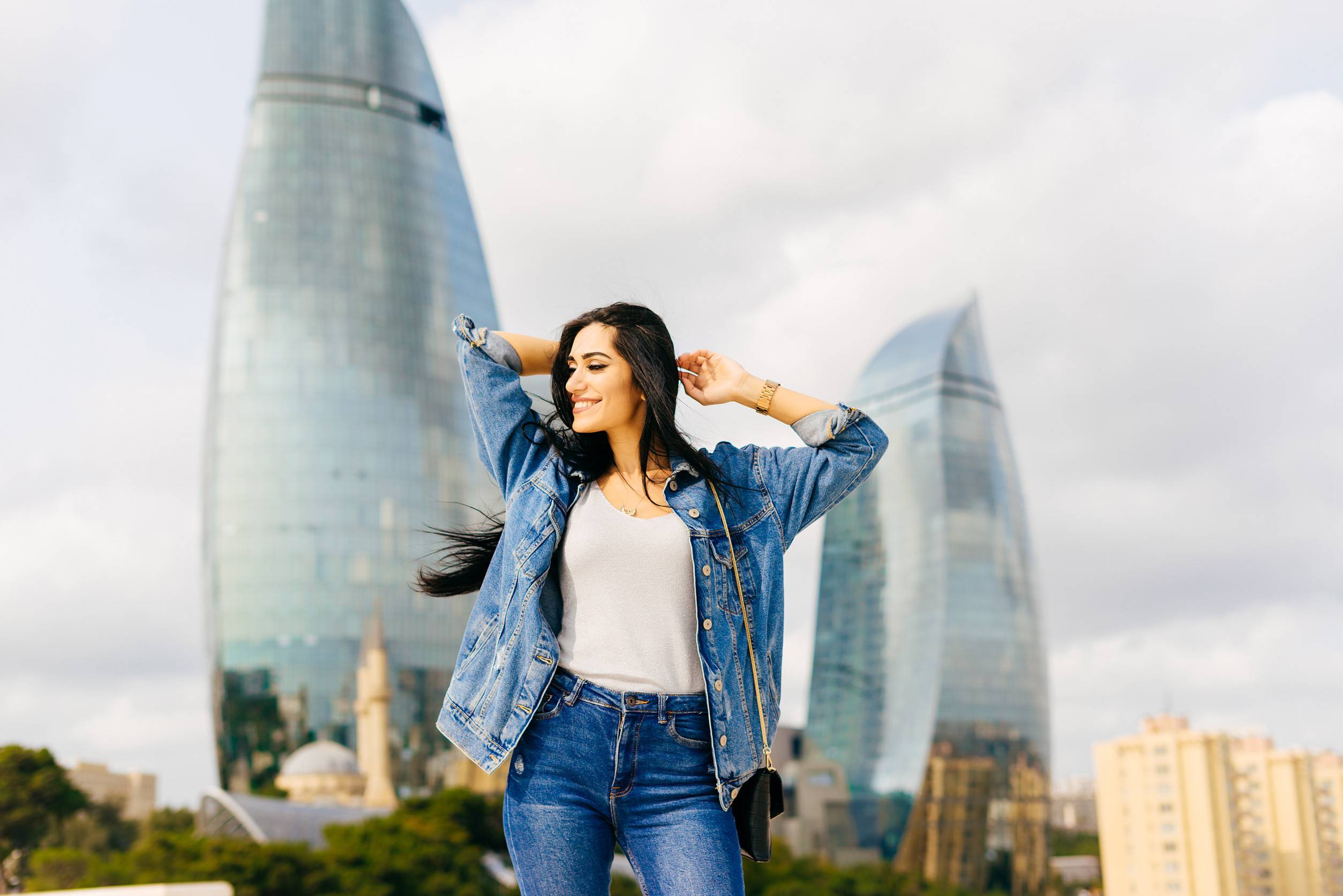 Una chica de cabello negro, alegre y elegante, camina por Azerbaiyán posando contra el fondo.