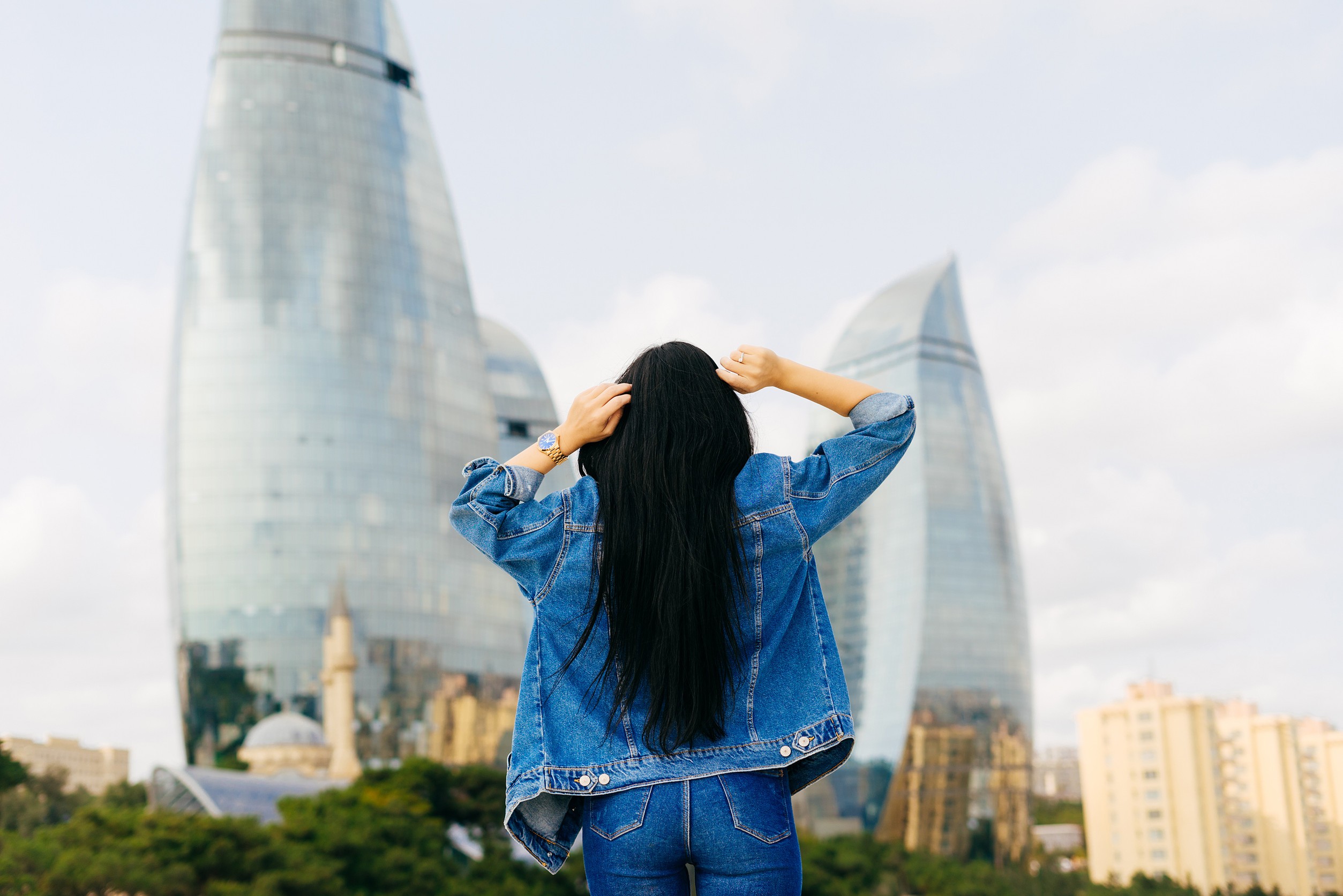 Ragazza bruna dai capelli lunghi viaggia in vacanza posando su uno sfondo di edifici moderni