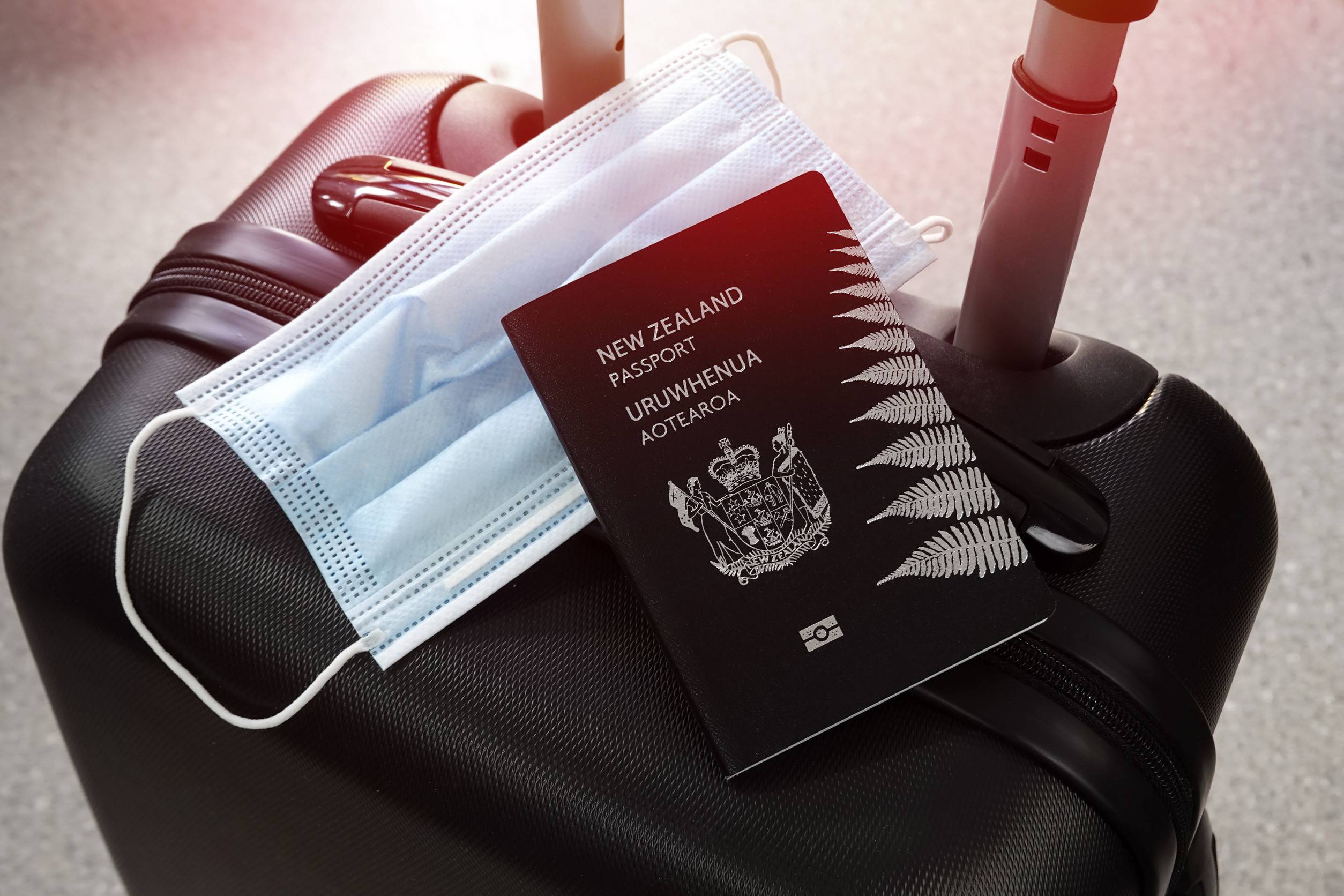 パンデミックのニュージーランド、黒いスーツケースに置かれたパスポートと防護マスク